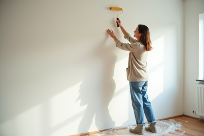 Femme en denim appliquant de la peinture blanche sur un mur